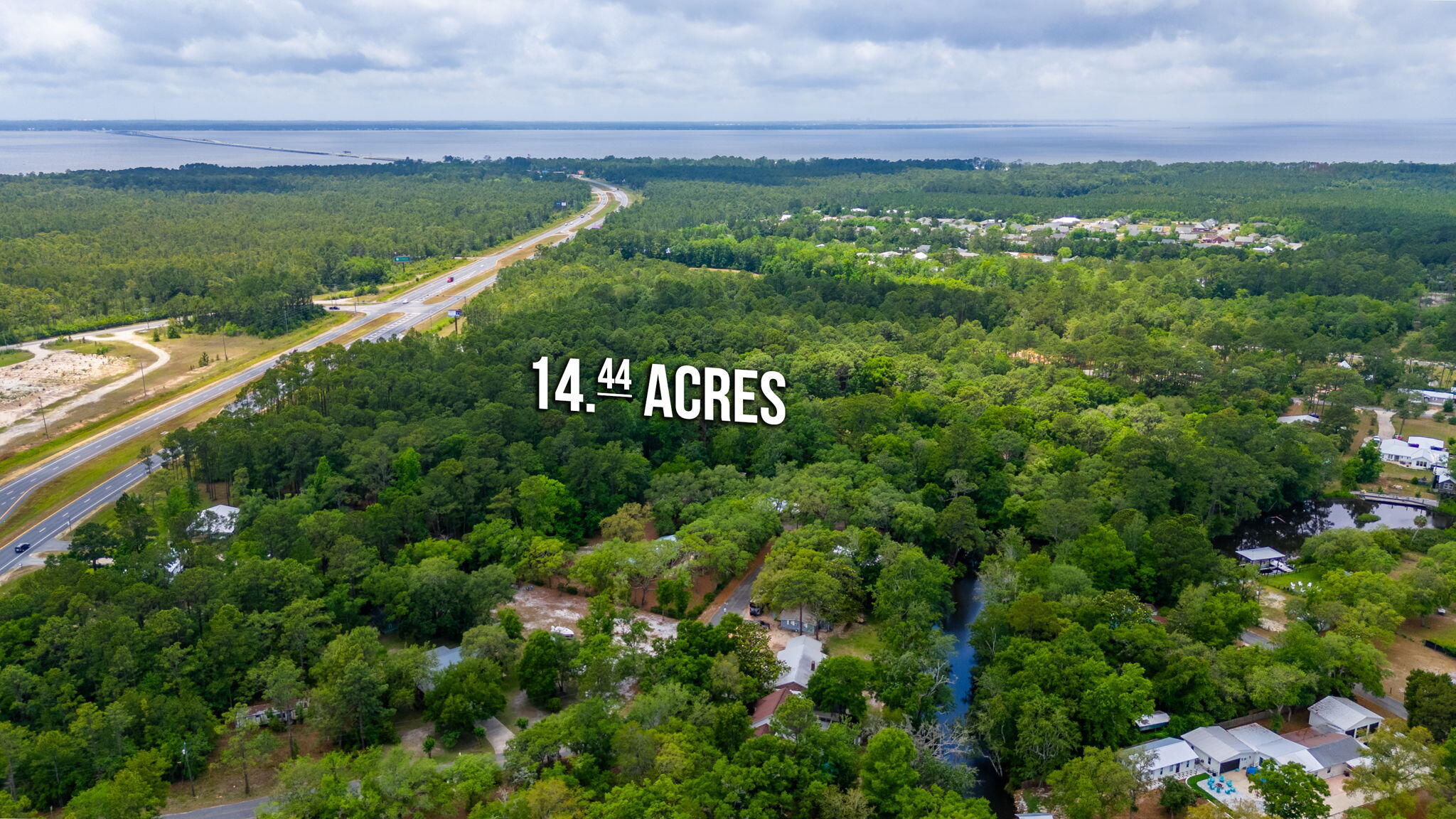 Aerial view of wooded acreage beside a highway, with a bay visible in the distance.