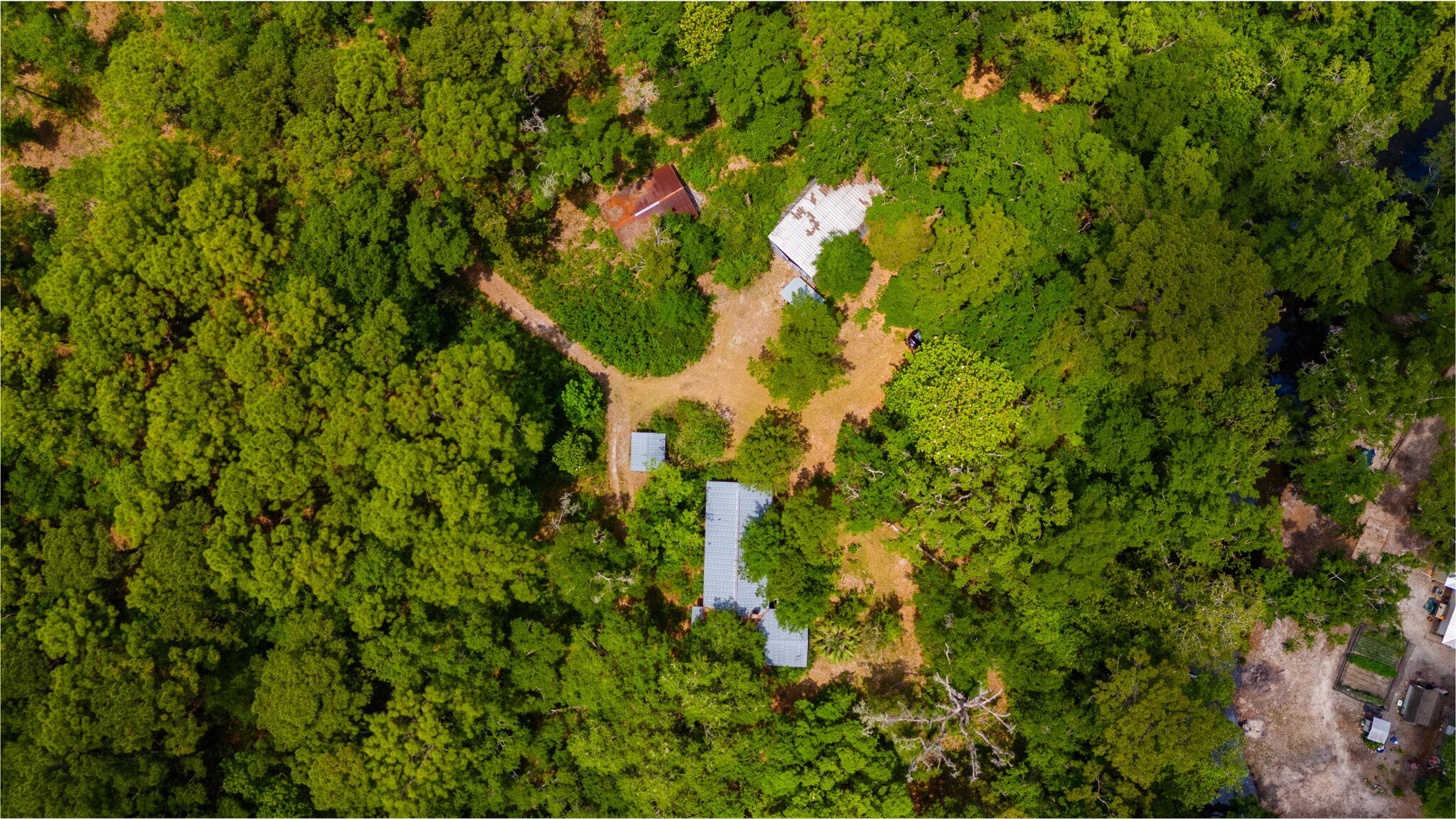 Aerial view of a wooded property with several buildings around a clearing and a narrow waterway.