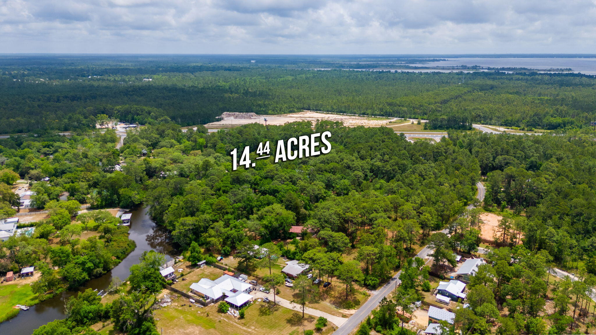 Aerial view of wooded 14.44-acre property near roads and water.