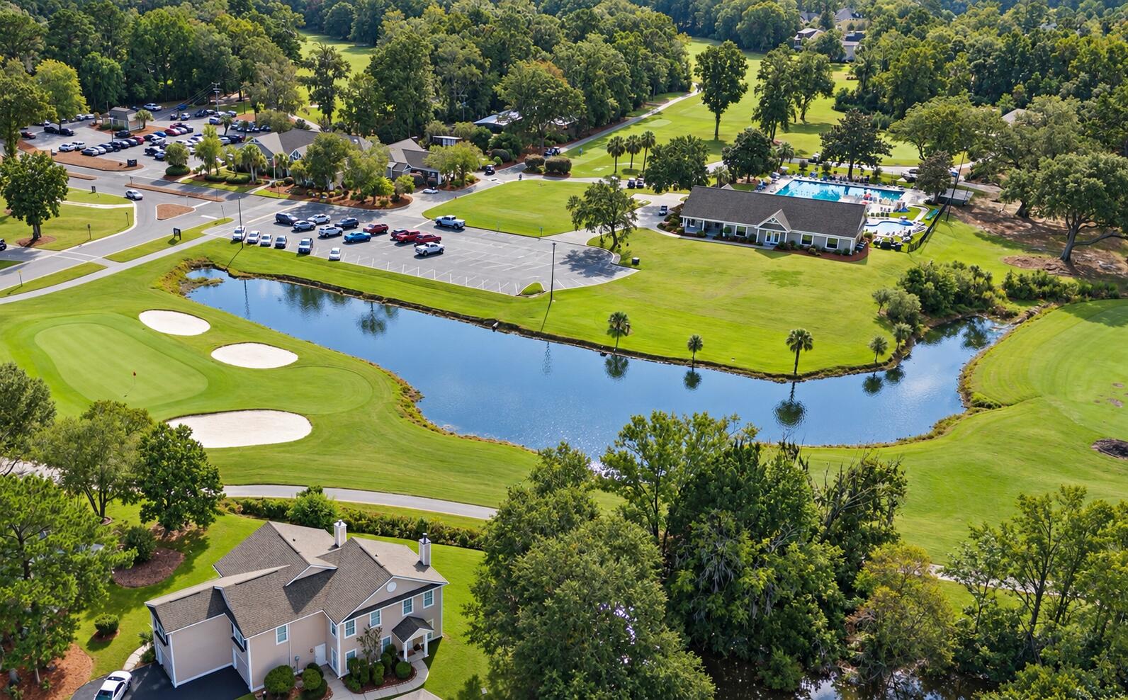 Aerial view of a home beside a golf course and pond, with a clubhouse and swimming pool.