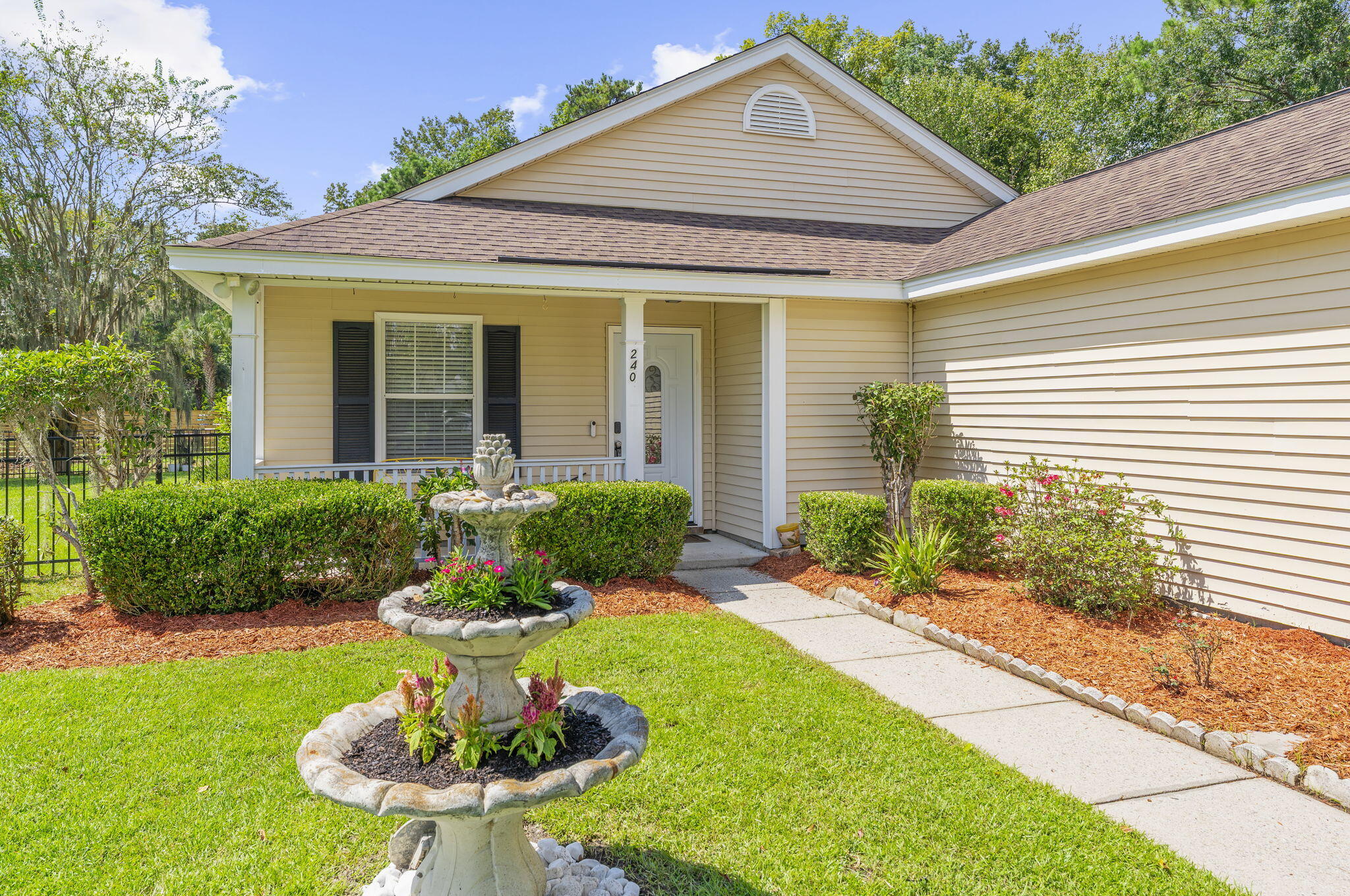 Home entrance with a covered porch, tiered stone fountain, and landscaped front garden.