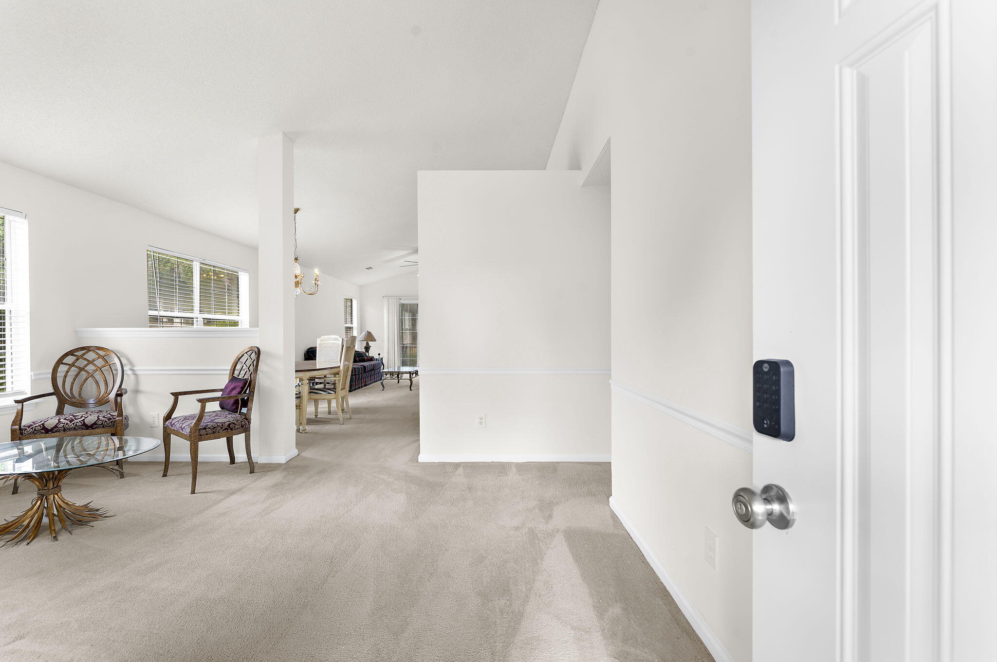 Carpeted entry sitting area with patterned chairs, glass table, and open front door with keypad lock.