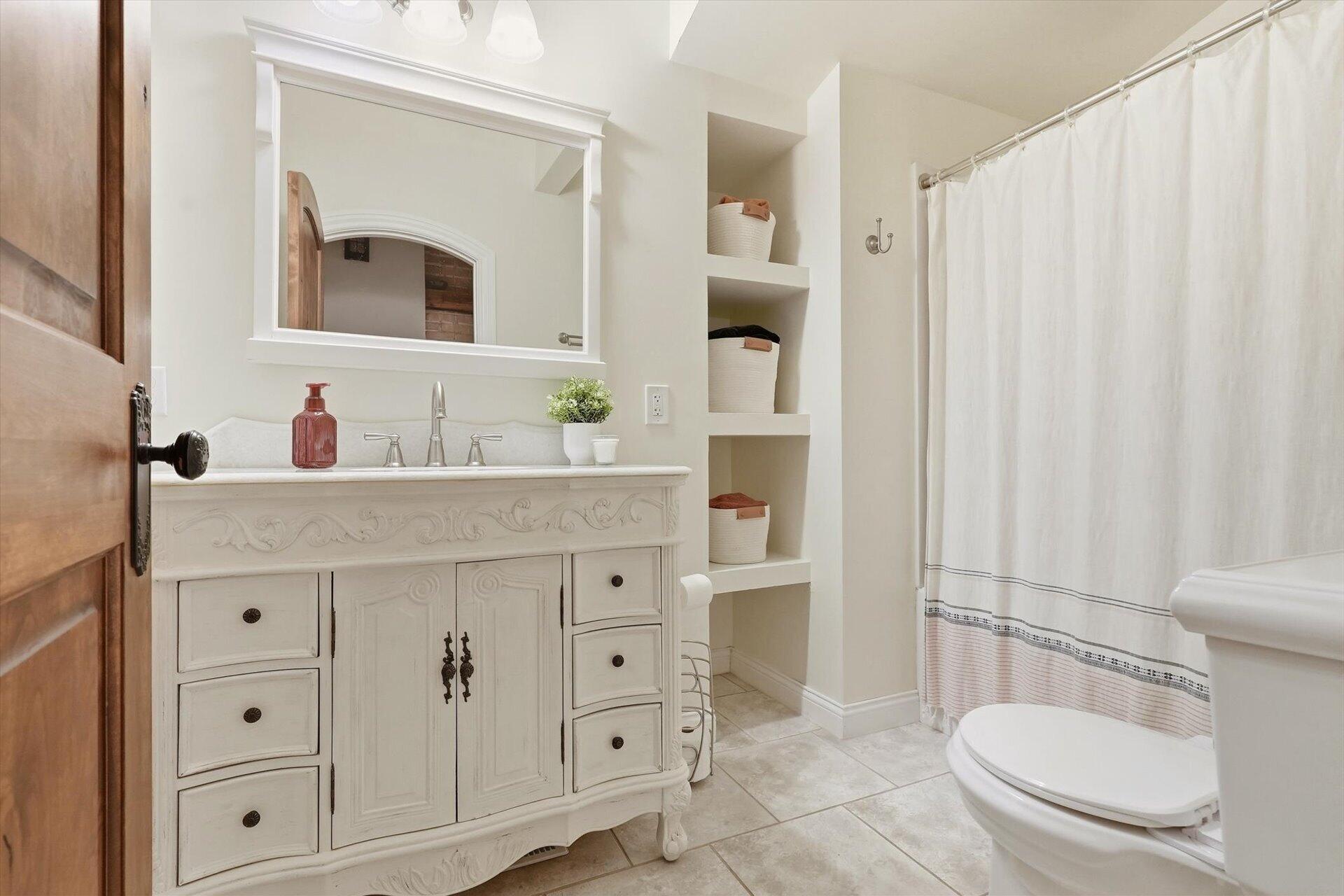 Bathroom with an ornate white vanity, built-in shelves, and a white shower curtain.