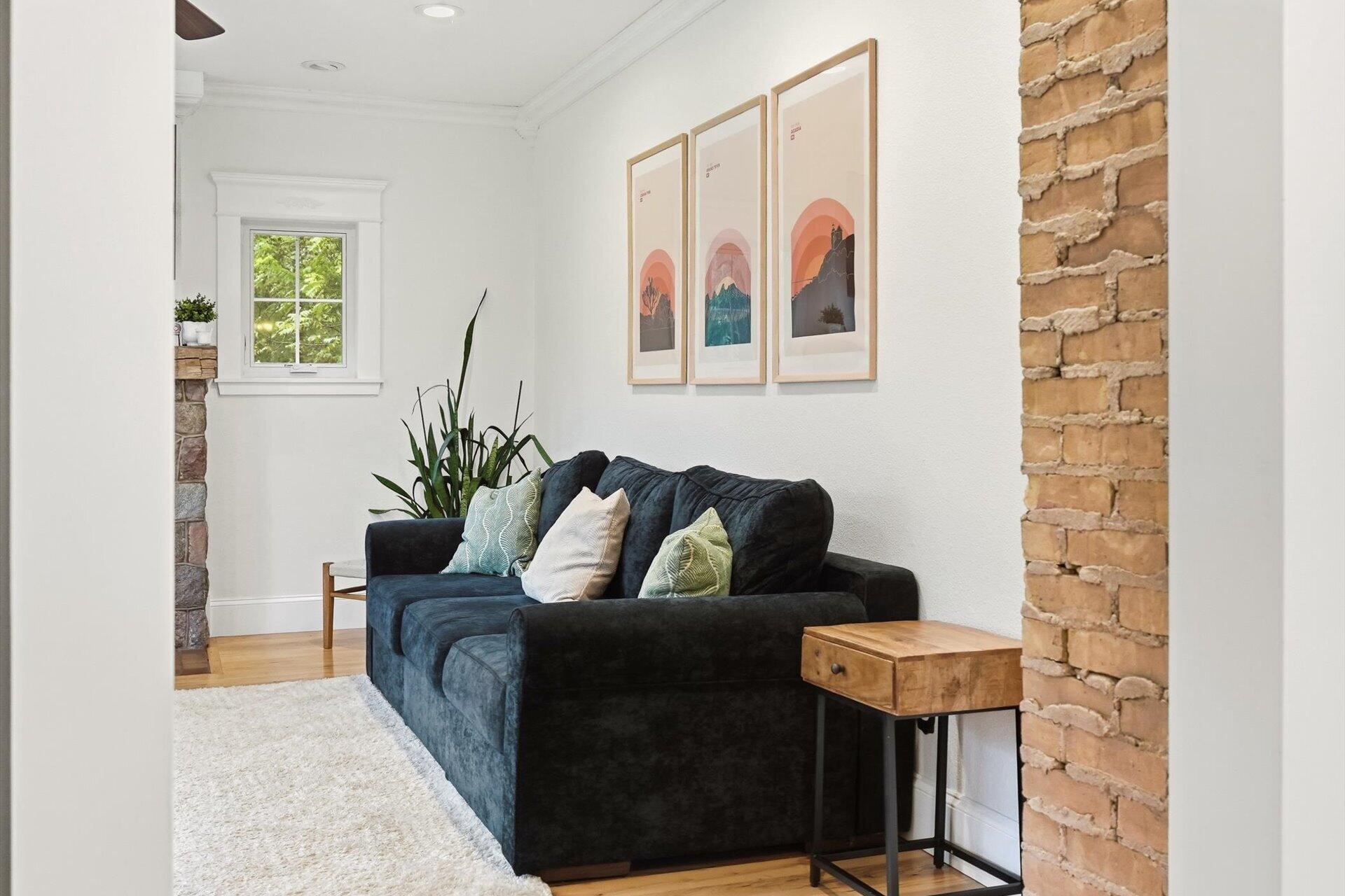 Living room with a dark blue sofa, framed prints, and an exposed brick wall.