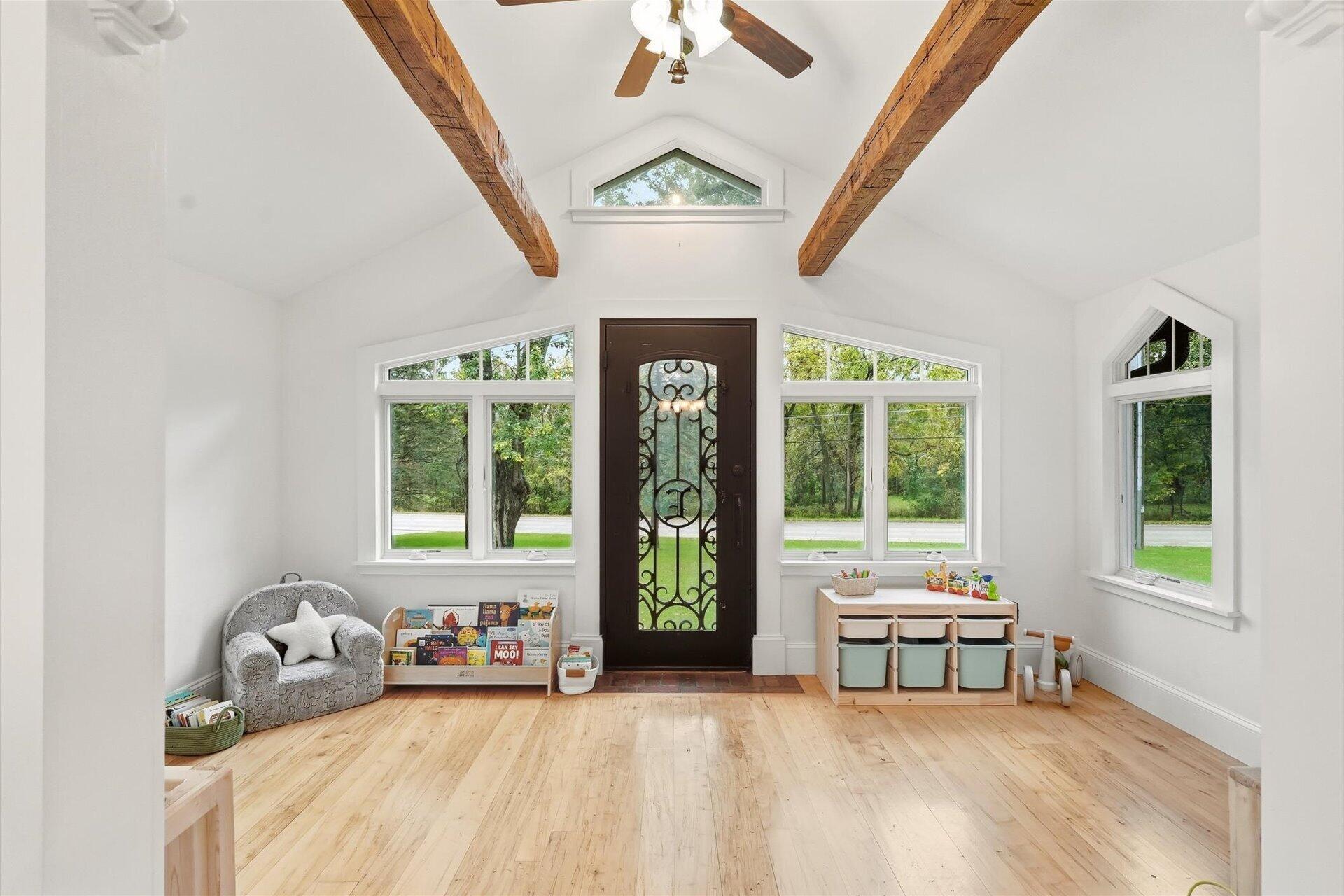 Bright entry room with exposed timber beams, tall windows, and a decorative glass front door.
