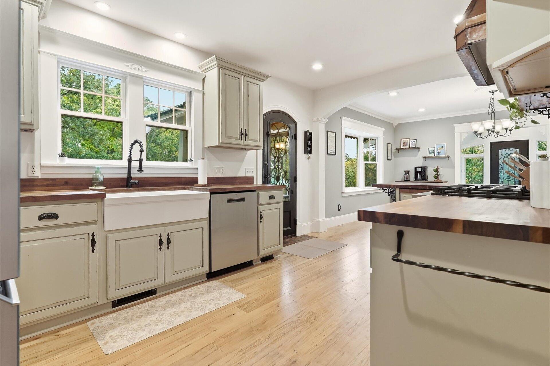 Bright kitchen with cream cabinets, butcher-block counters, farmhouse sink, and a large cooktop island.