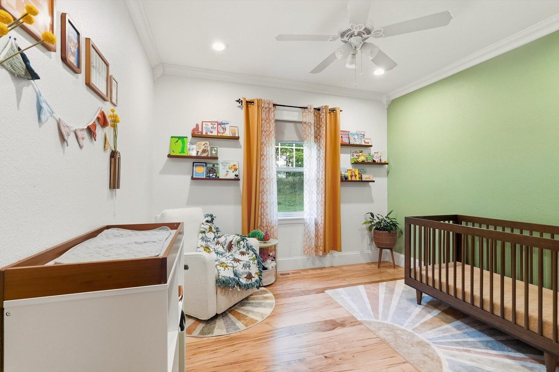 Nursery with a dark wood crib, white changing table, orange curtains, and children's books on wall shelves.