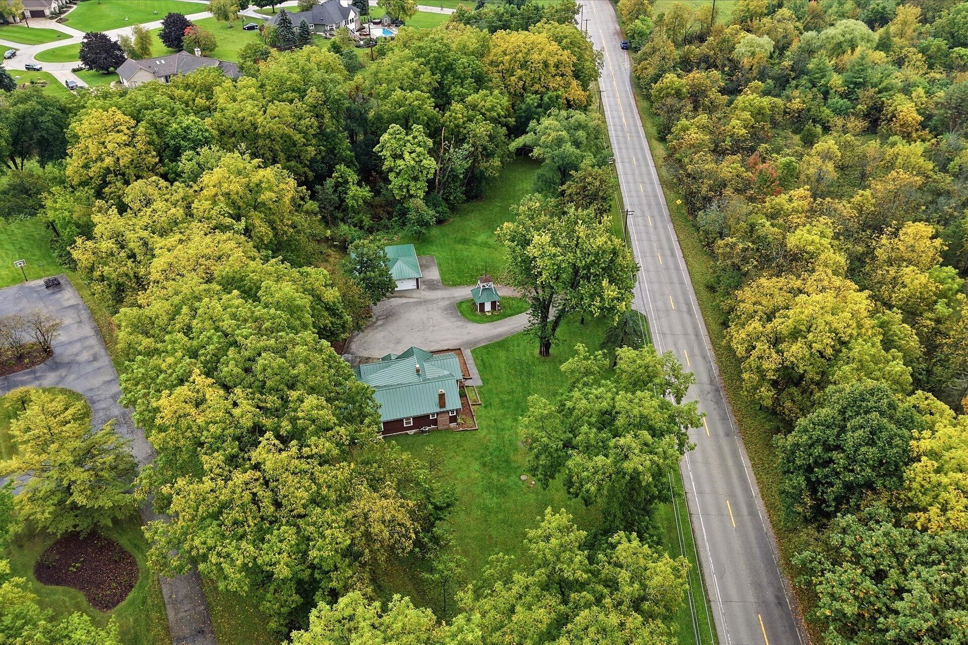 Aerial view of a wooded property with green-roofed buildings beside a two-lane road.