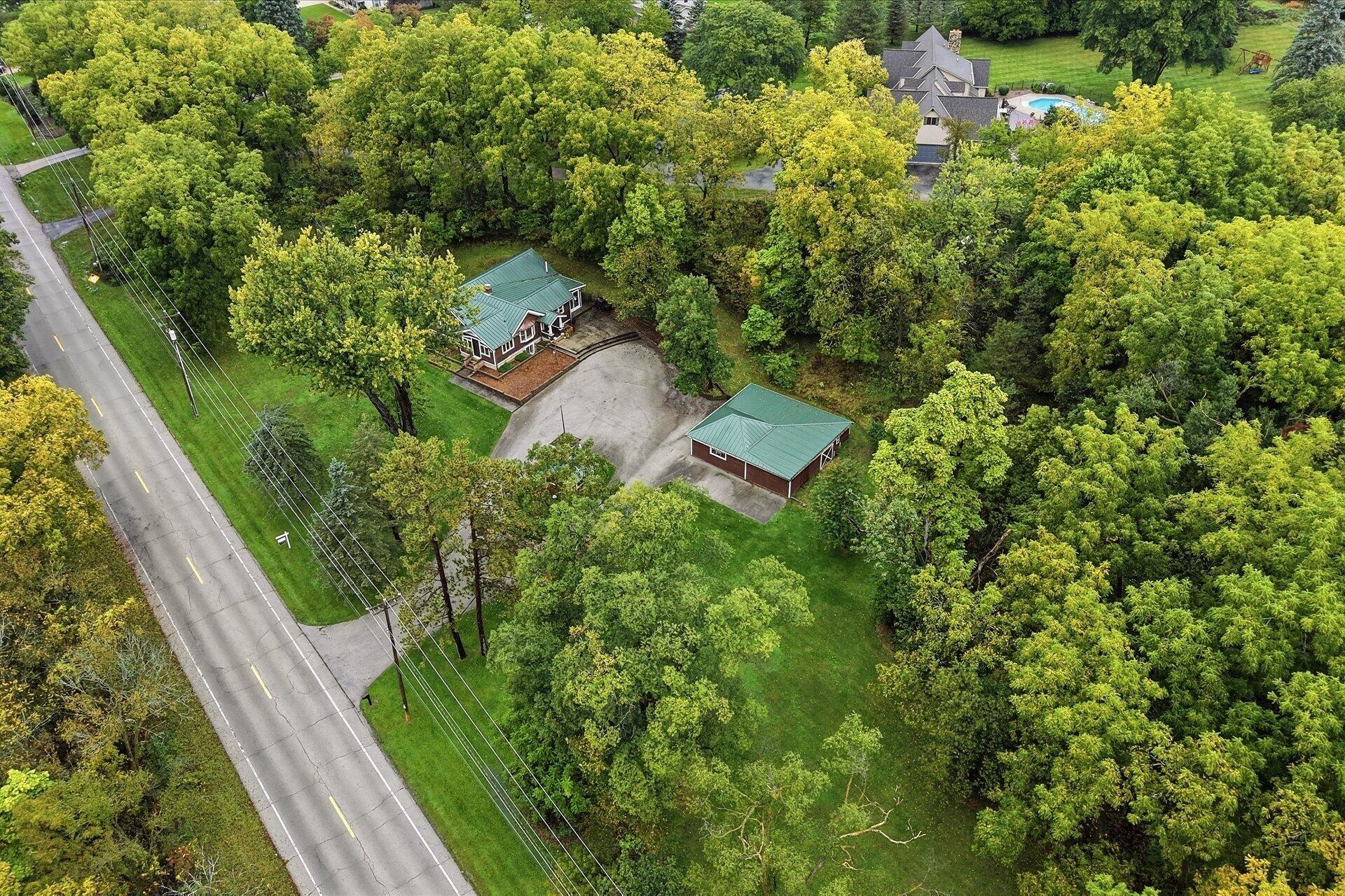 Aerial view of a green-roofed home and detached outbuilding amid mature trees.