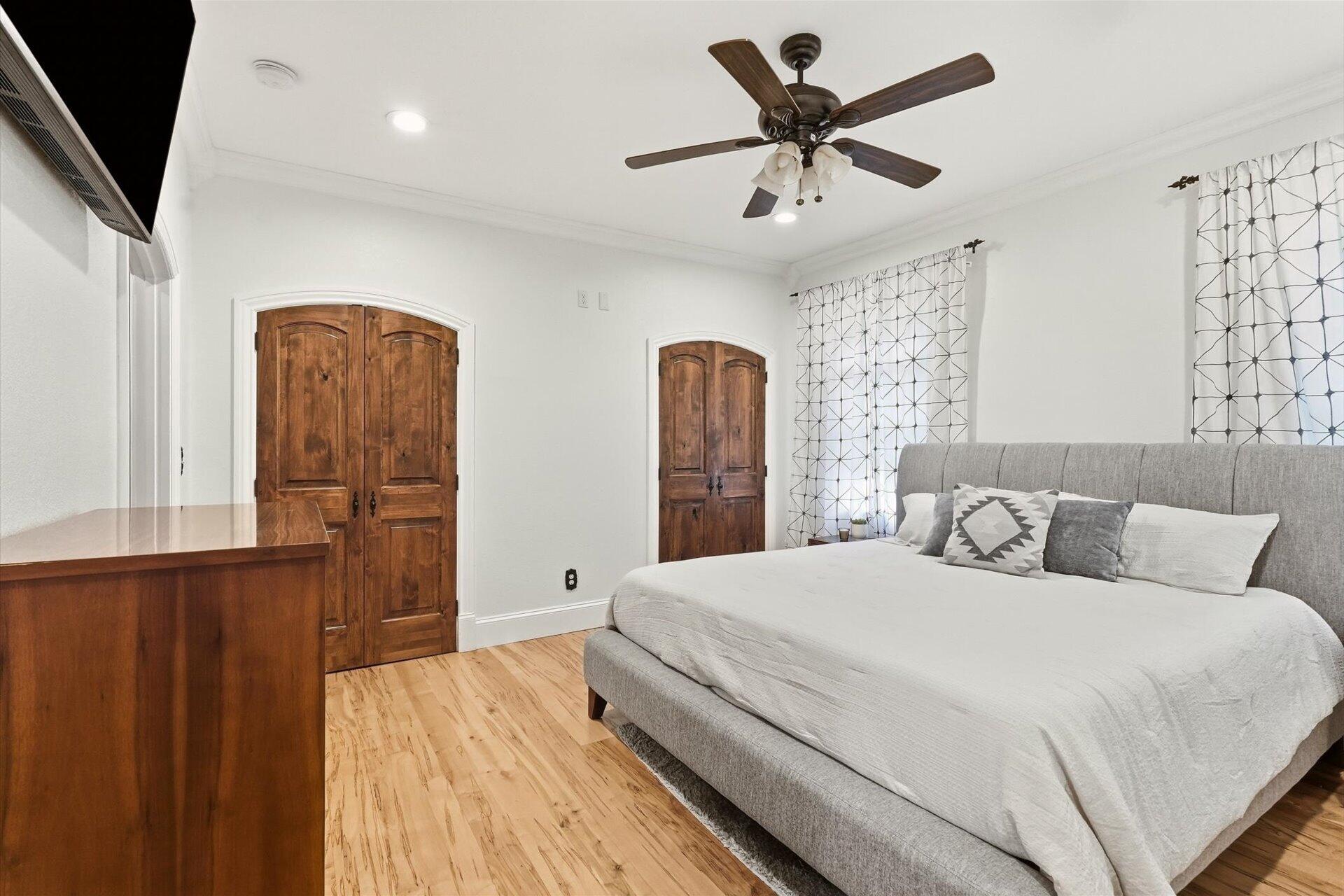 Bedroom with a gray upholstered bed, hardwood floors, and two arched wooden doors.