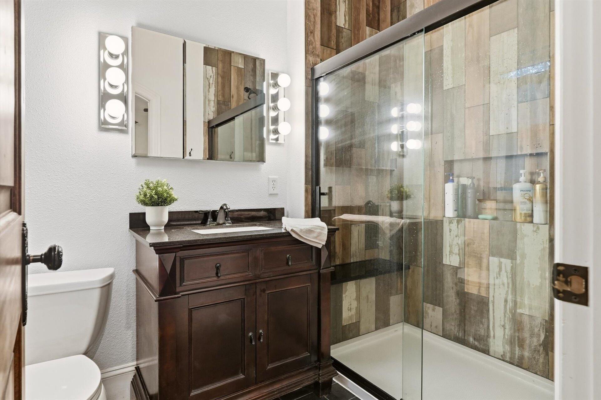 Bathroom with a dark wood vanity and glass shower lined with multicolored wood-look tile.
