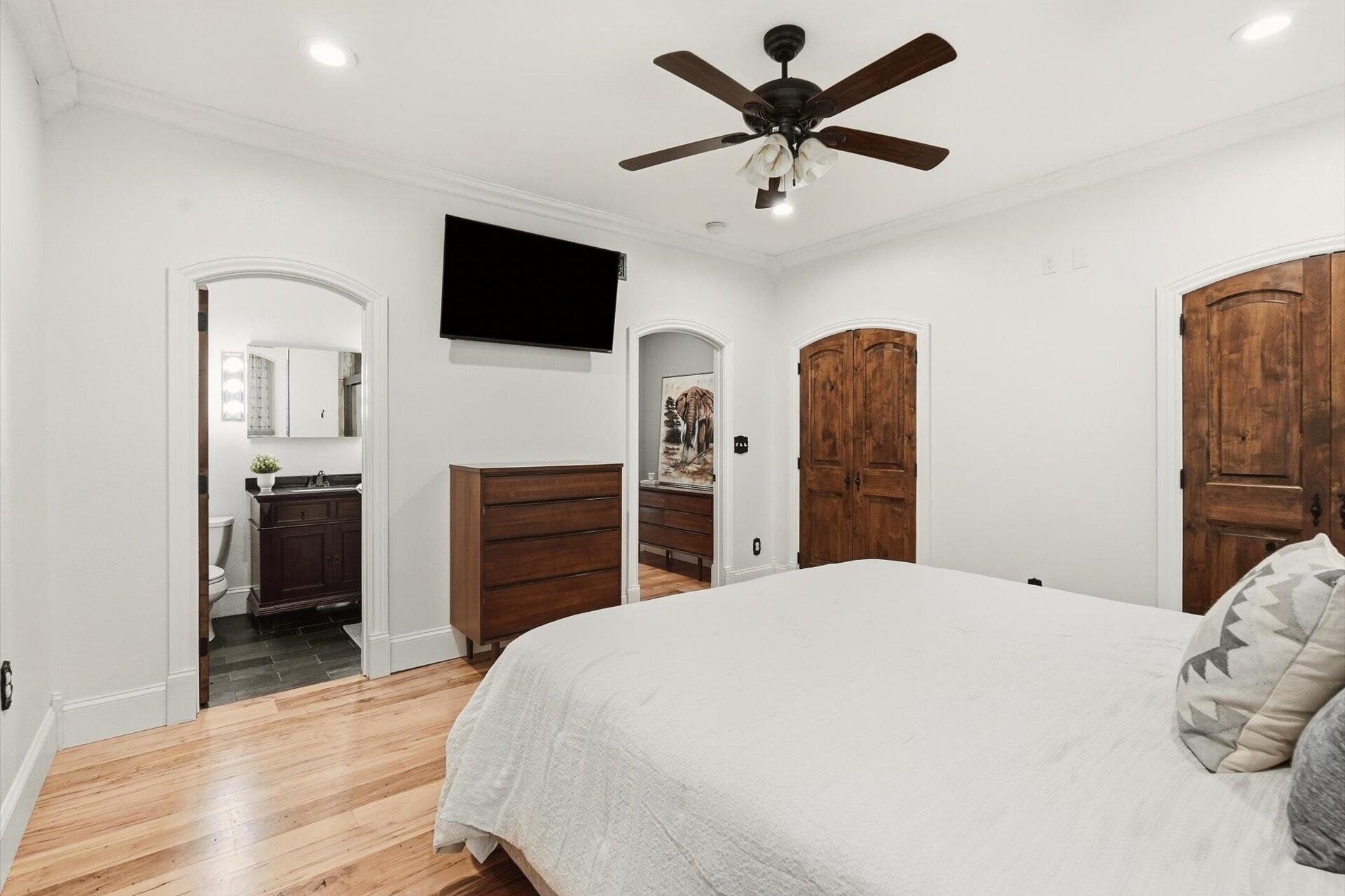 Bedroom with a large bed, hardwood floors, dark wood doors, and an arched ensuite bathroom doorway.