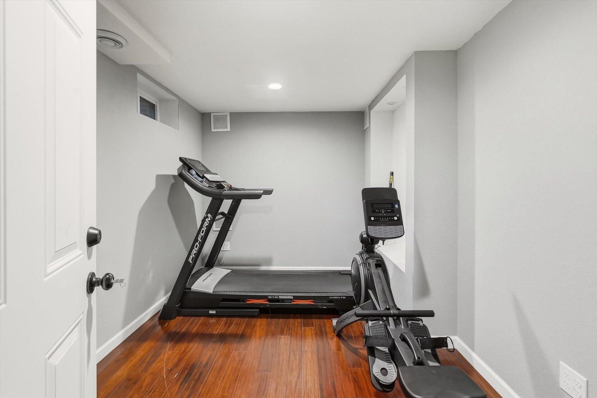 Basement gym with a treadmill and elliptical on polished wood flooring.