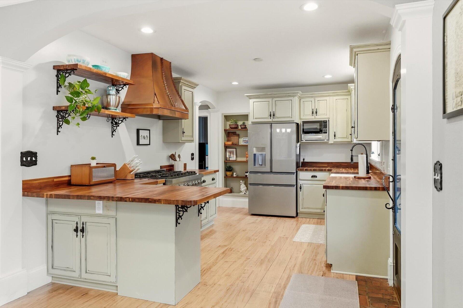 Kitchen with a large butcher-block island, cream cabinets, stainless steel appliances, and a copper range hood.