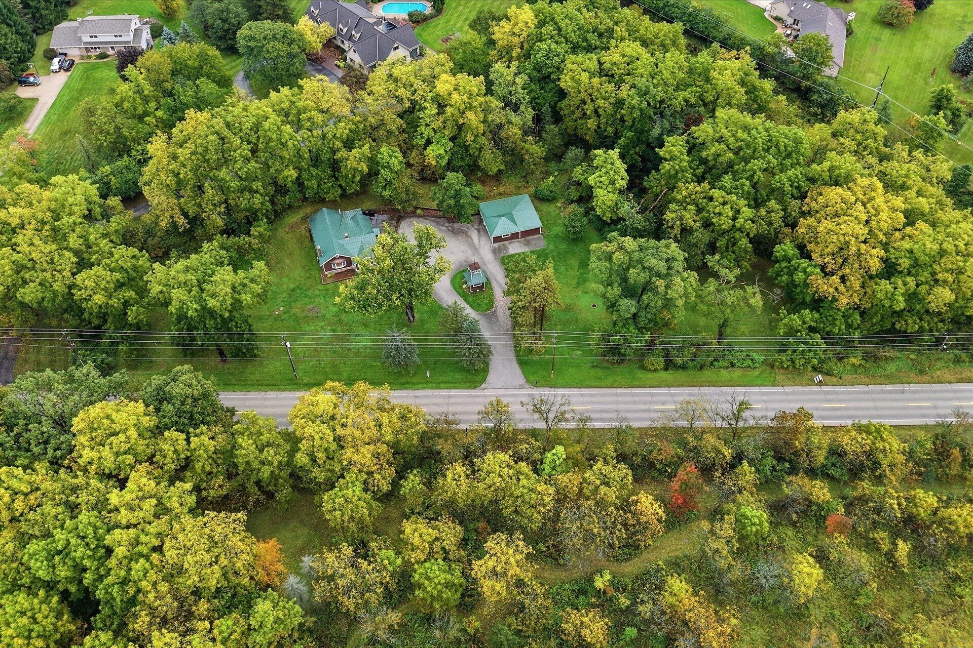 Aerial view of a wooded property with a green-roofed house and detached outbuilding.