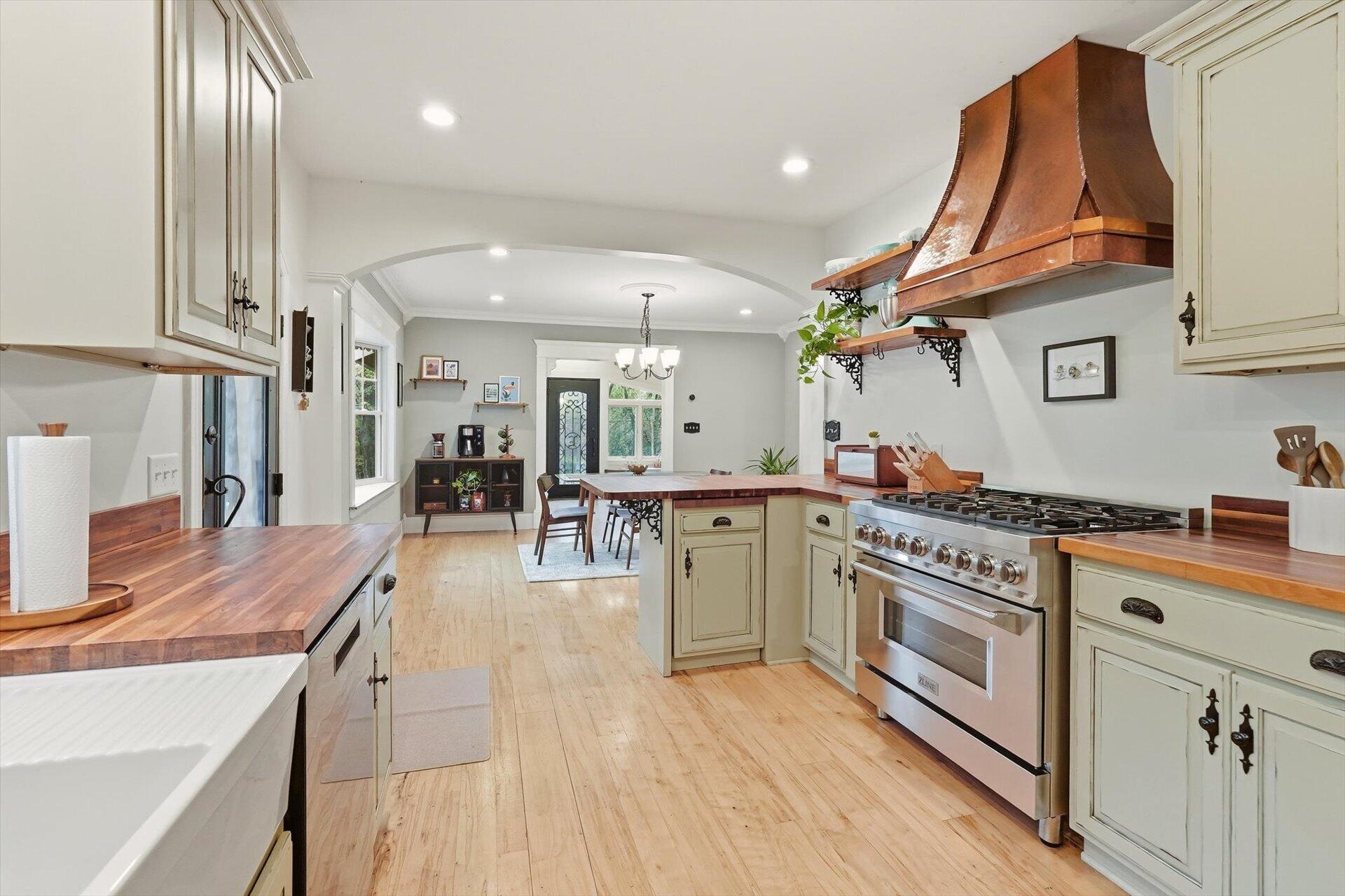 Kitchen with butcher-block counters, a copper range hood, and stainless steel range beside an arched dining area.