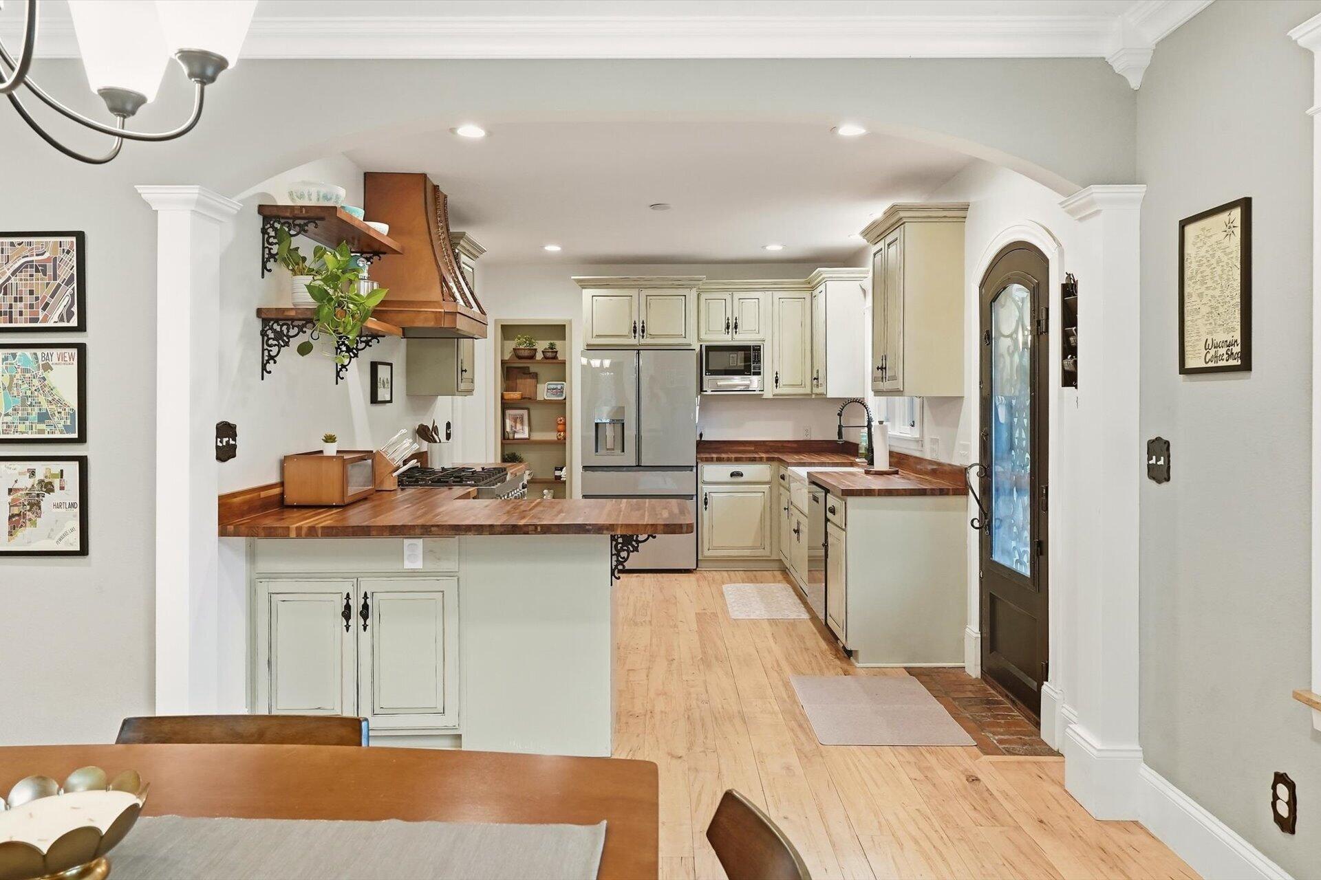 Kitchen with cream cabinetry, butcher-block counters, stainless appliances, and a copper range hood.
