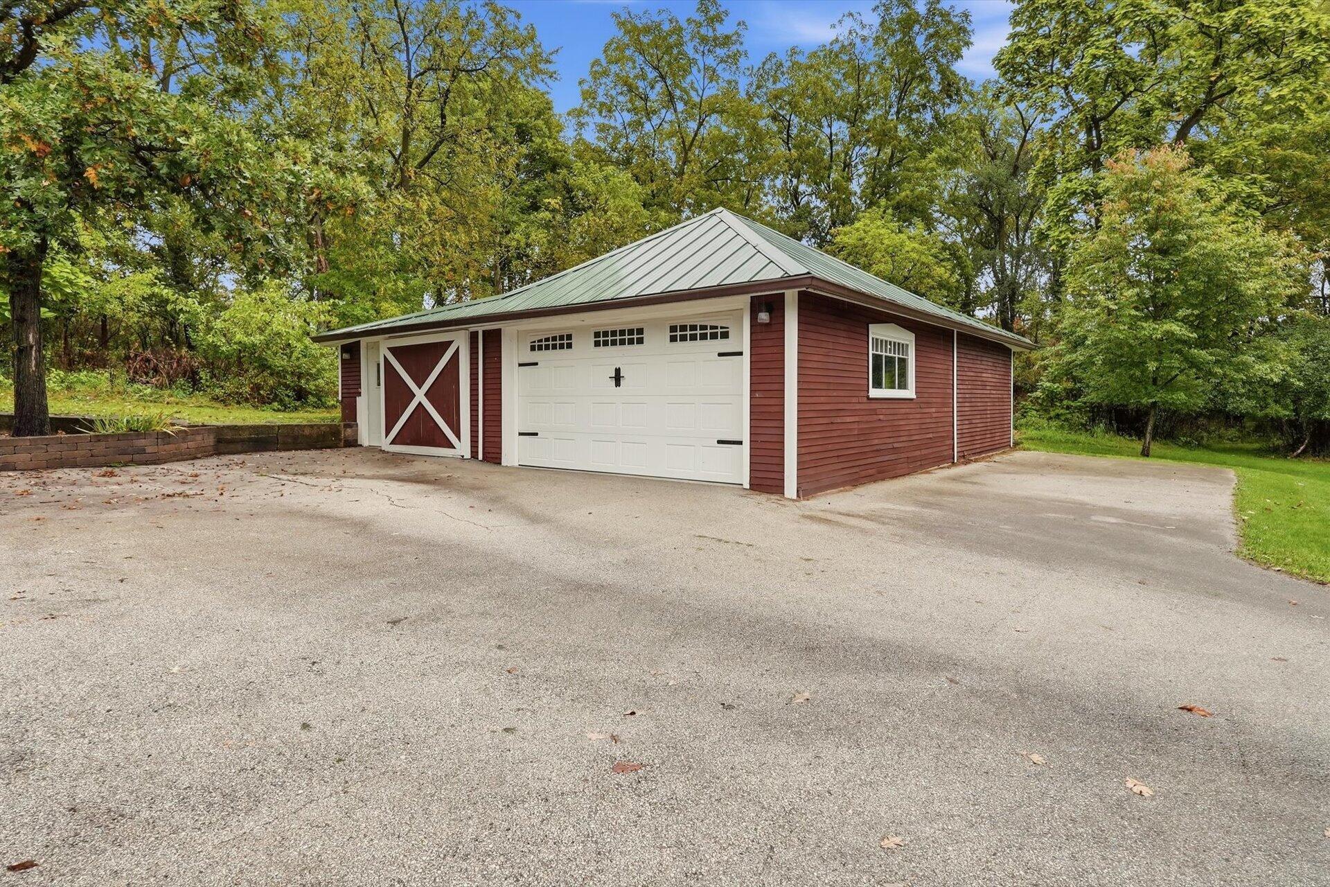 Detached red garage with a green metal roof and white doors beside a broad paved driveway.
