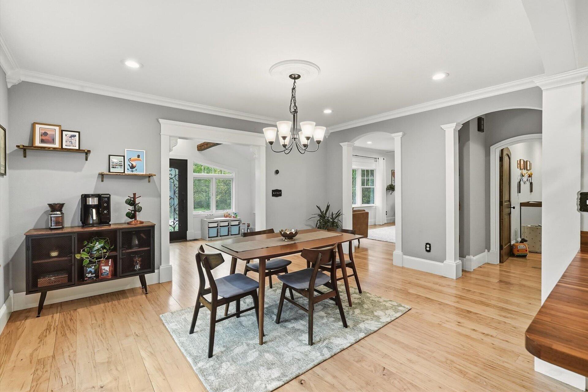 Dining room with a wooden table, patterned rug, hardwood floors, and chandelier.