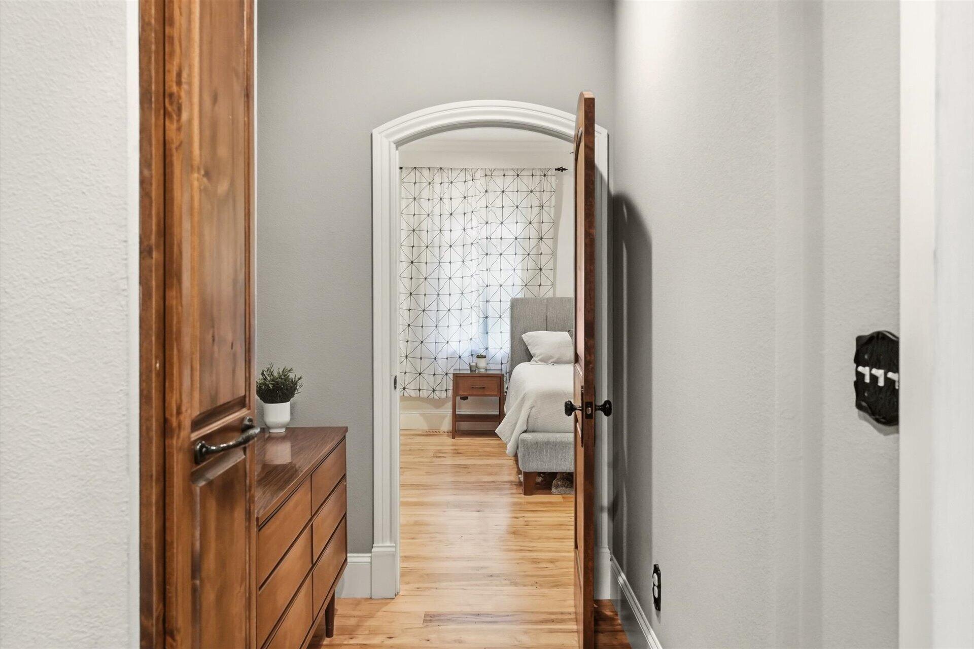 Bedroom with a gray upholstered bed and geometric curtains, viewed through an arched doorway.