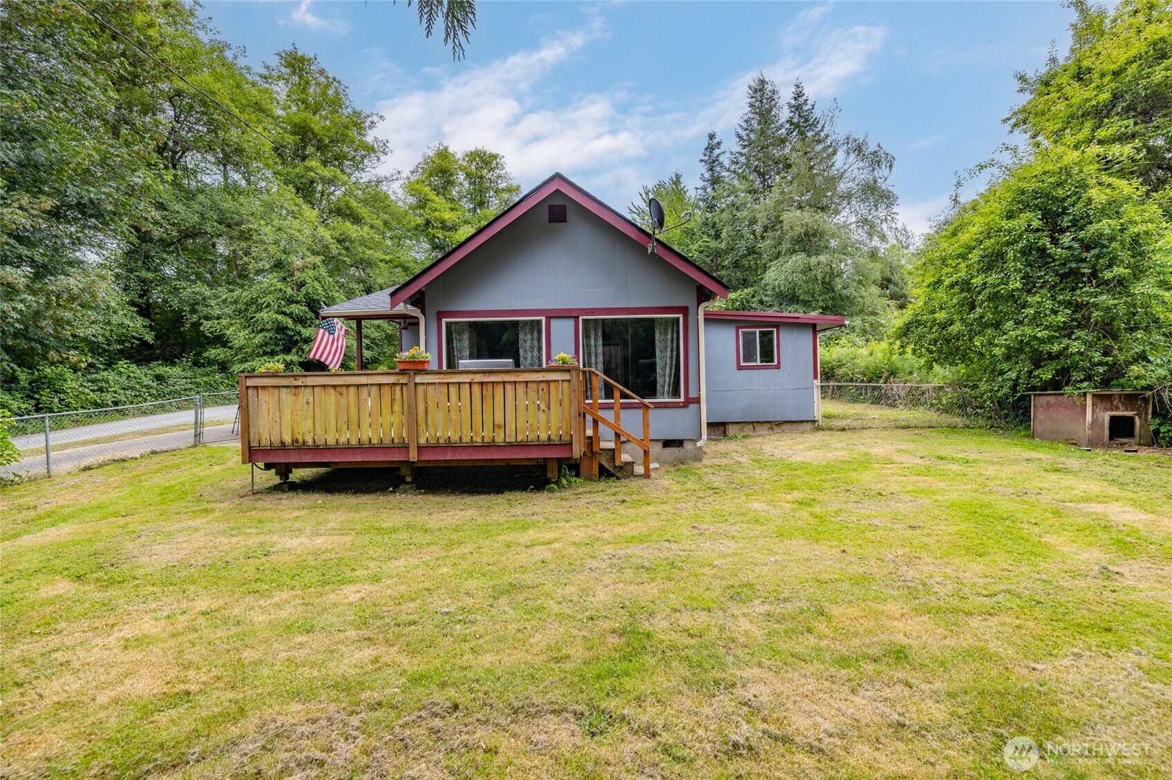Gray house with burgundy trim and a raised wooden deck in a tree-lined grassy yard.