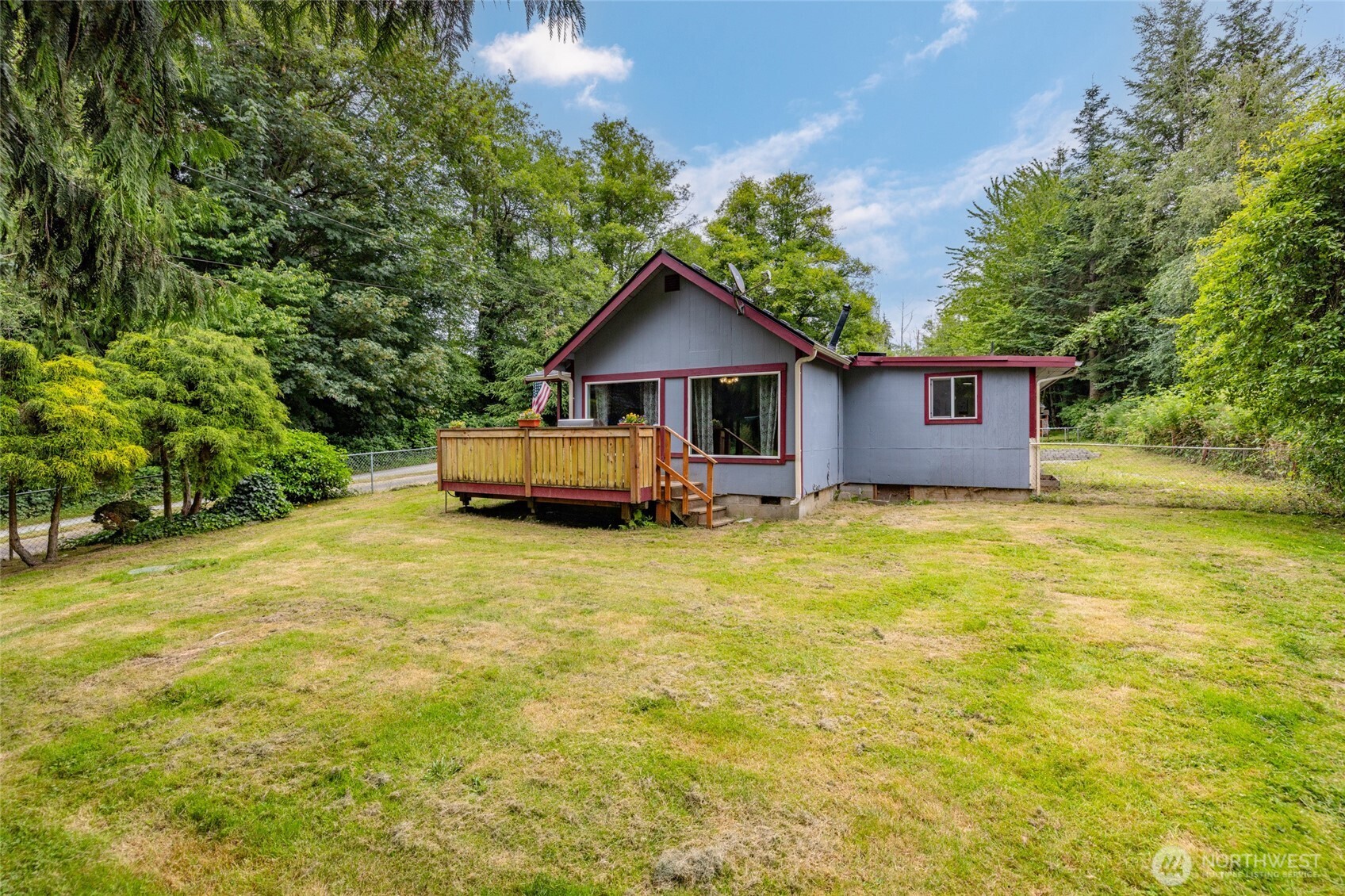 Gray house with red trim and raised wooden deck in a grassy, tree-lined yard.