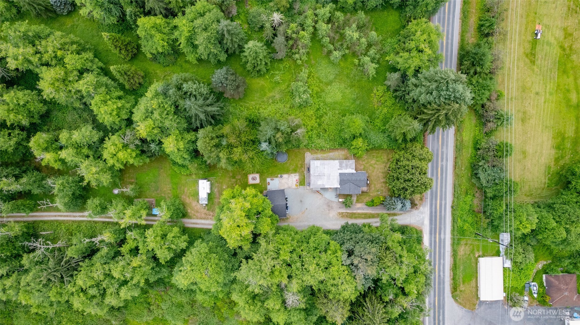 Aerial view of a wooded property with a house, outbuildings, and gravel driveway beside a road.