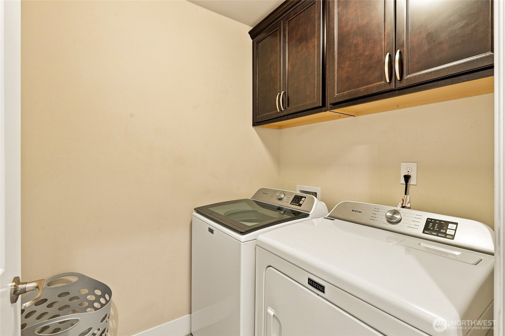 Laundry room with a top-loading washer and dryer beneath dark wood cabinets.