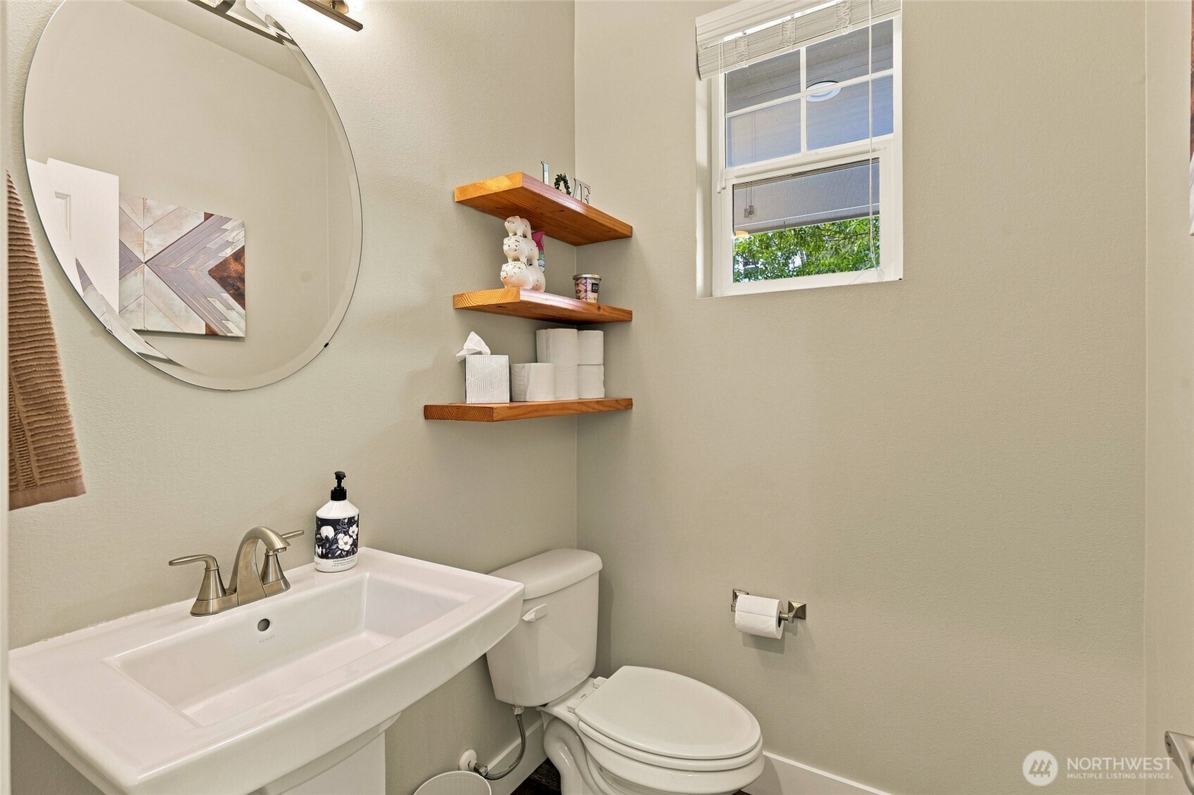 Bathroom with a white vanity, toilet, round mirror, and wooden floating shelves.
