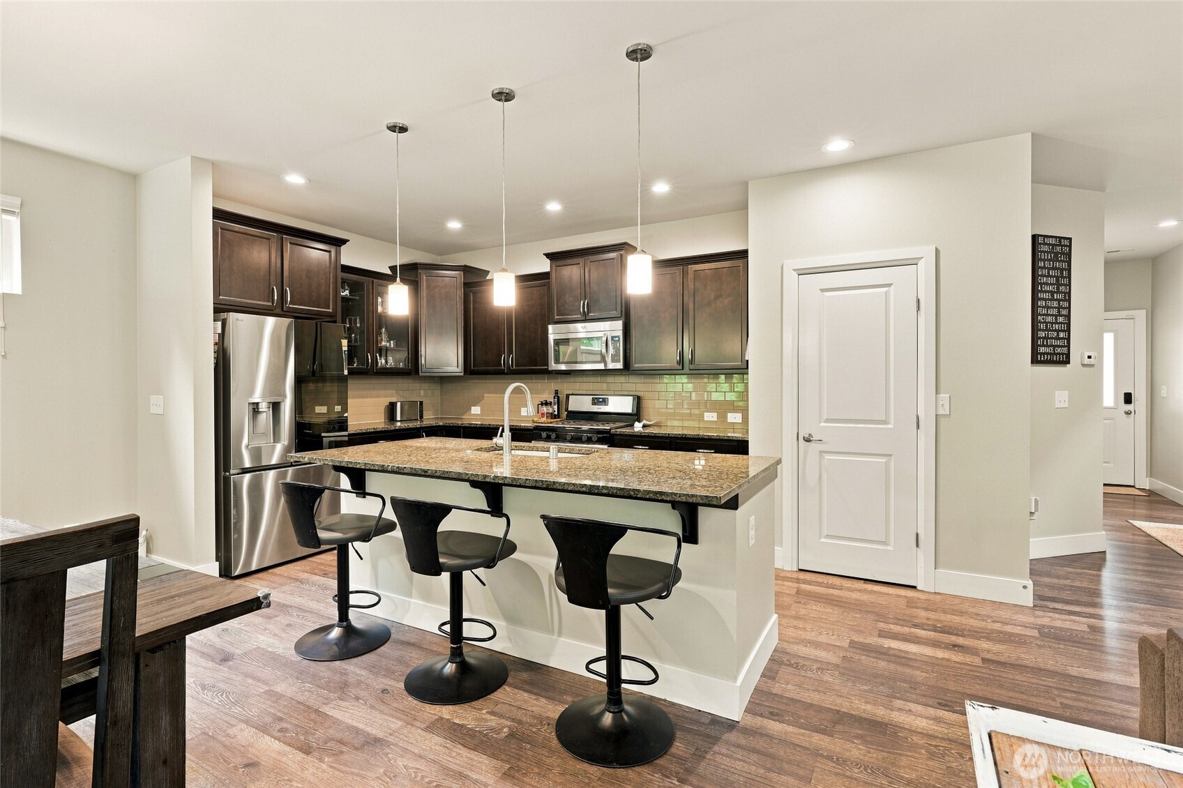 Kitchen with dark cabinets, stainless appliances, granite island, and three bar stools.