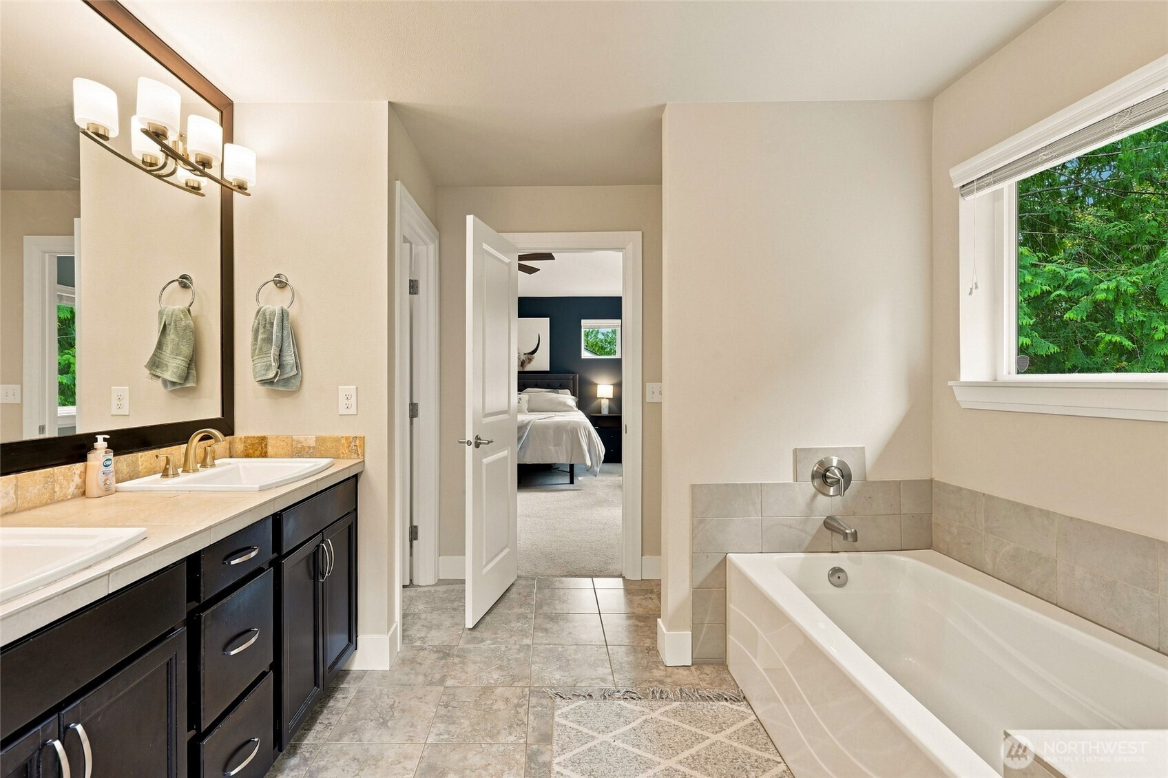 Bathroom with a soaking tub beside a window and a dark double vanity.