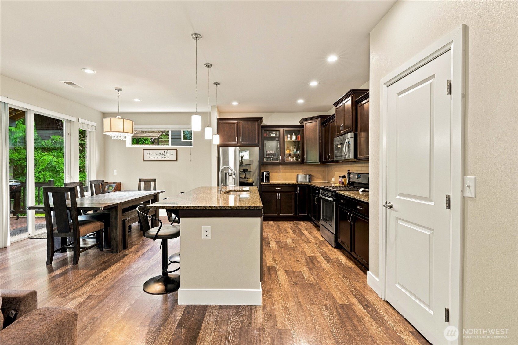 Kitchen and dining area with a granite island, dark cabinets, and windows overlooking greenery.