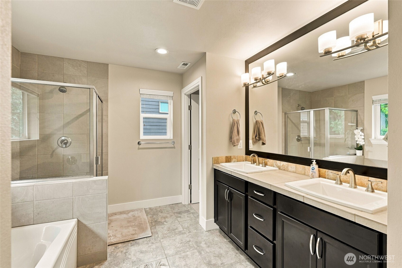 Bathroom with tiled glass shower, bathtub, and dark double-sink vanity.