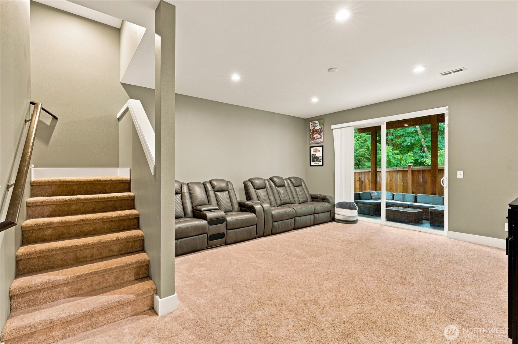 Carpeted media room with reclining theater seats, a staircase, and sliding doors to a wooded patio.