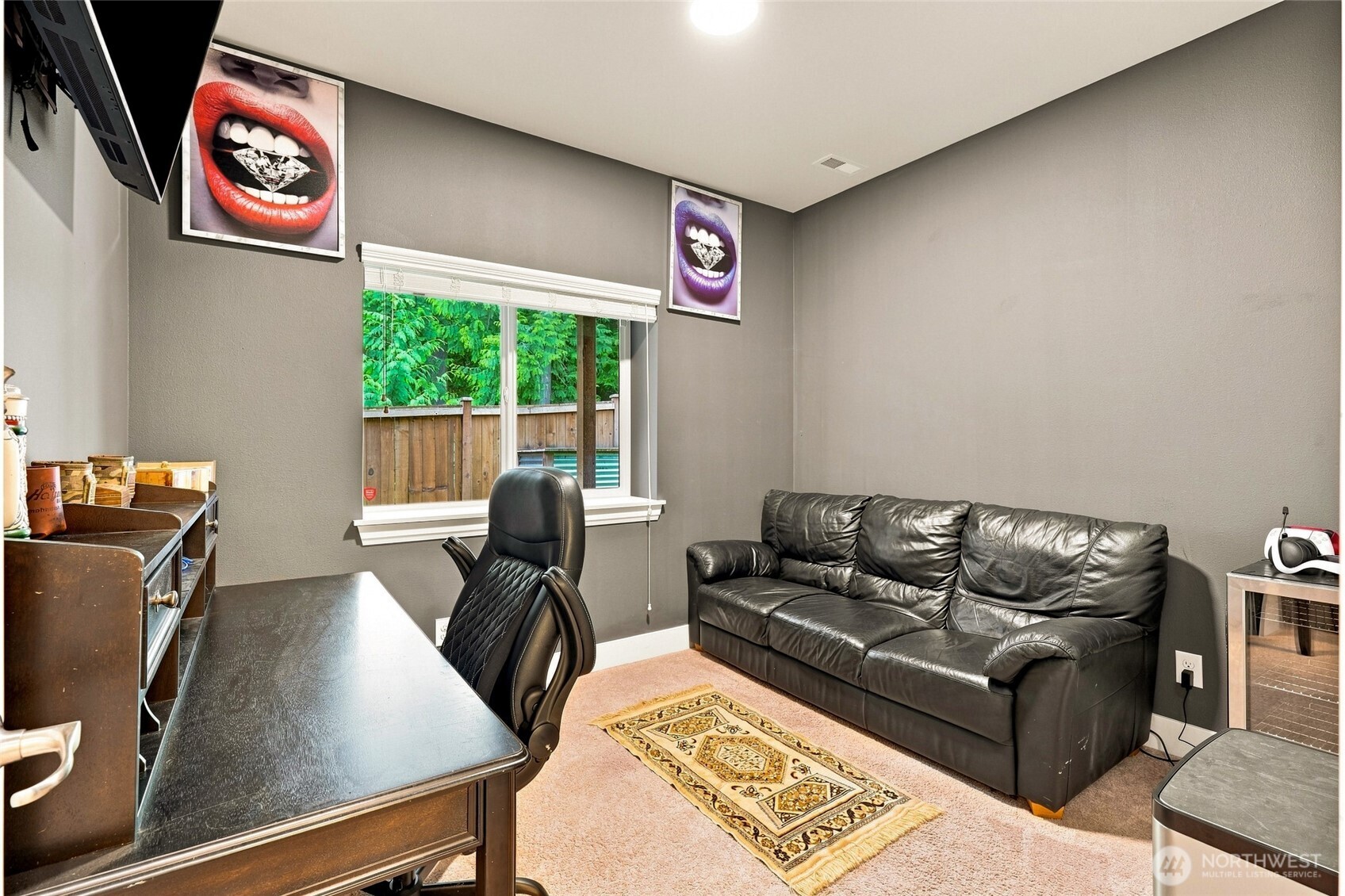 Furnished home office with a black leather sofa, desk, and window overlooking greenery and a pool.