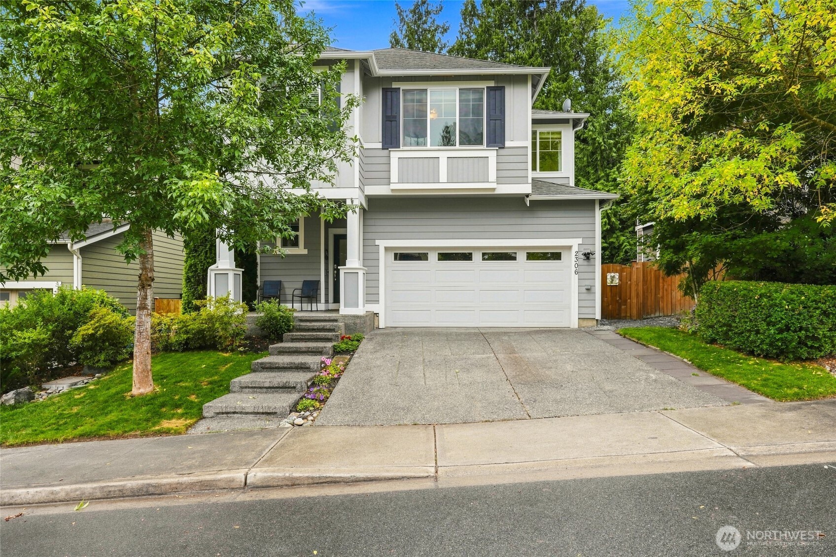 Two-story gray house with a double garage, covered porch, and leafy landscaped front yard.