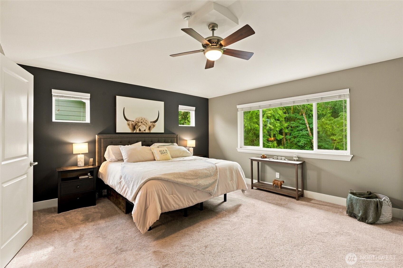 Furnished bedroom with a charcoal accent wall and a large window overlooking green trees.
