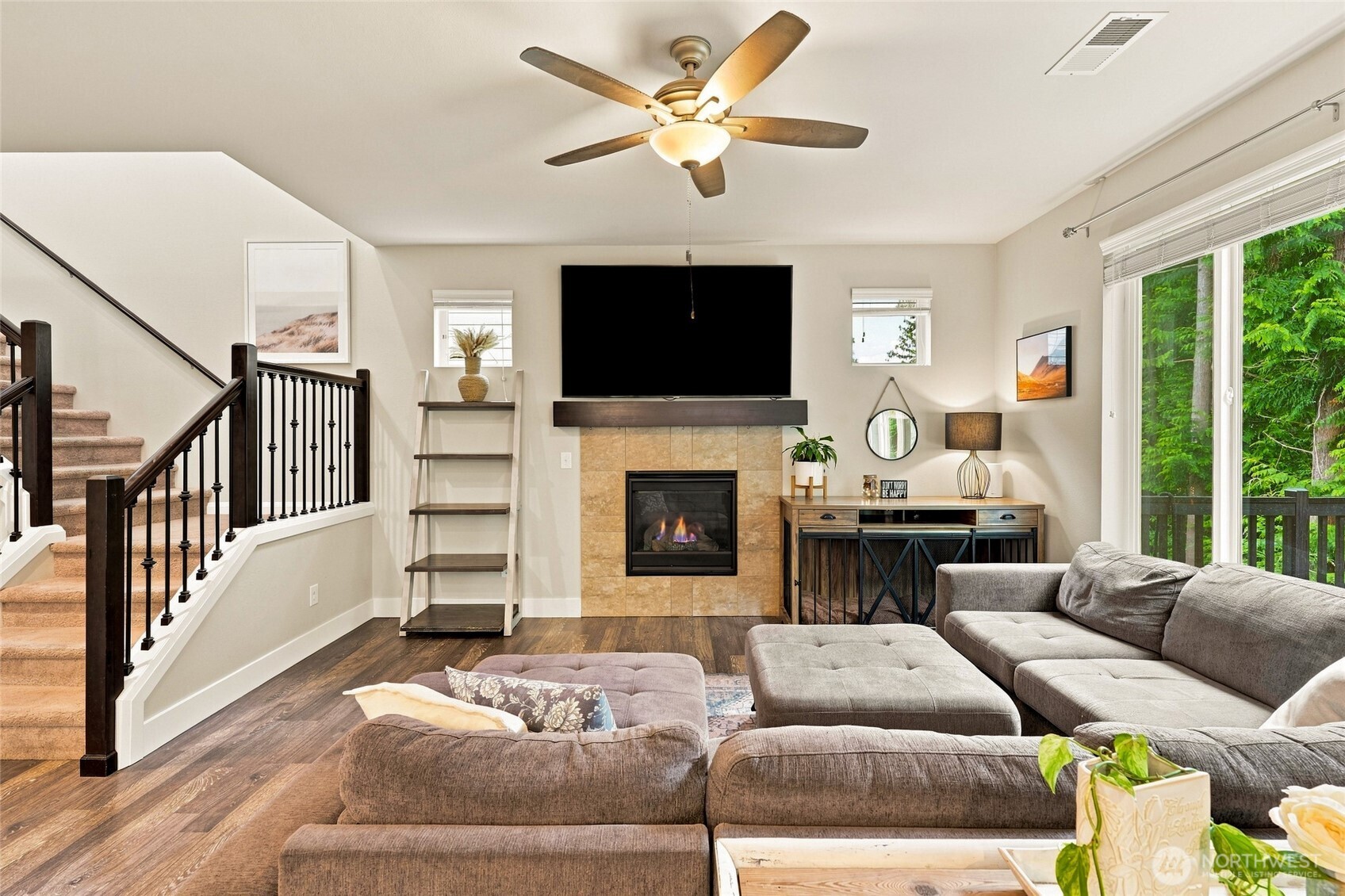 Living room with a stone-tile fireplace, gray sectional, and staircase beside sliding glass doors.