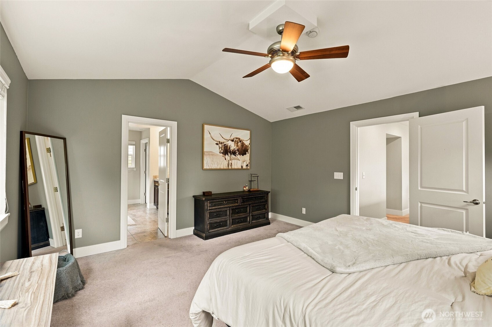 Bedroom with vaulted ceiling, gray walls, ceiling fan, dark dresser, and white bedding.