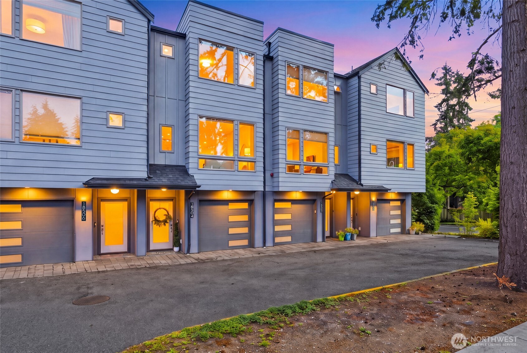 Modern blue-gray townhomes with illuminated windows and garages at dusk.