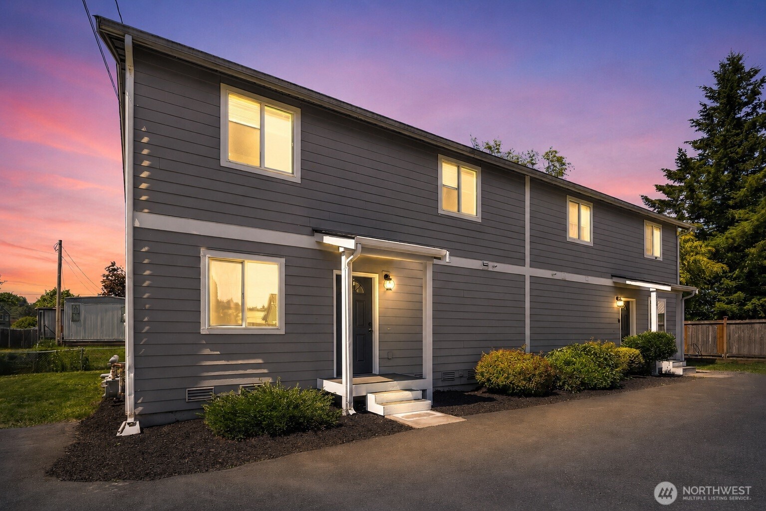Gray two-story residence with covered entrances and lit windows at sunset.