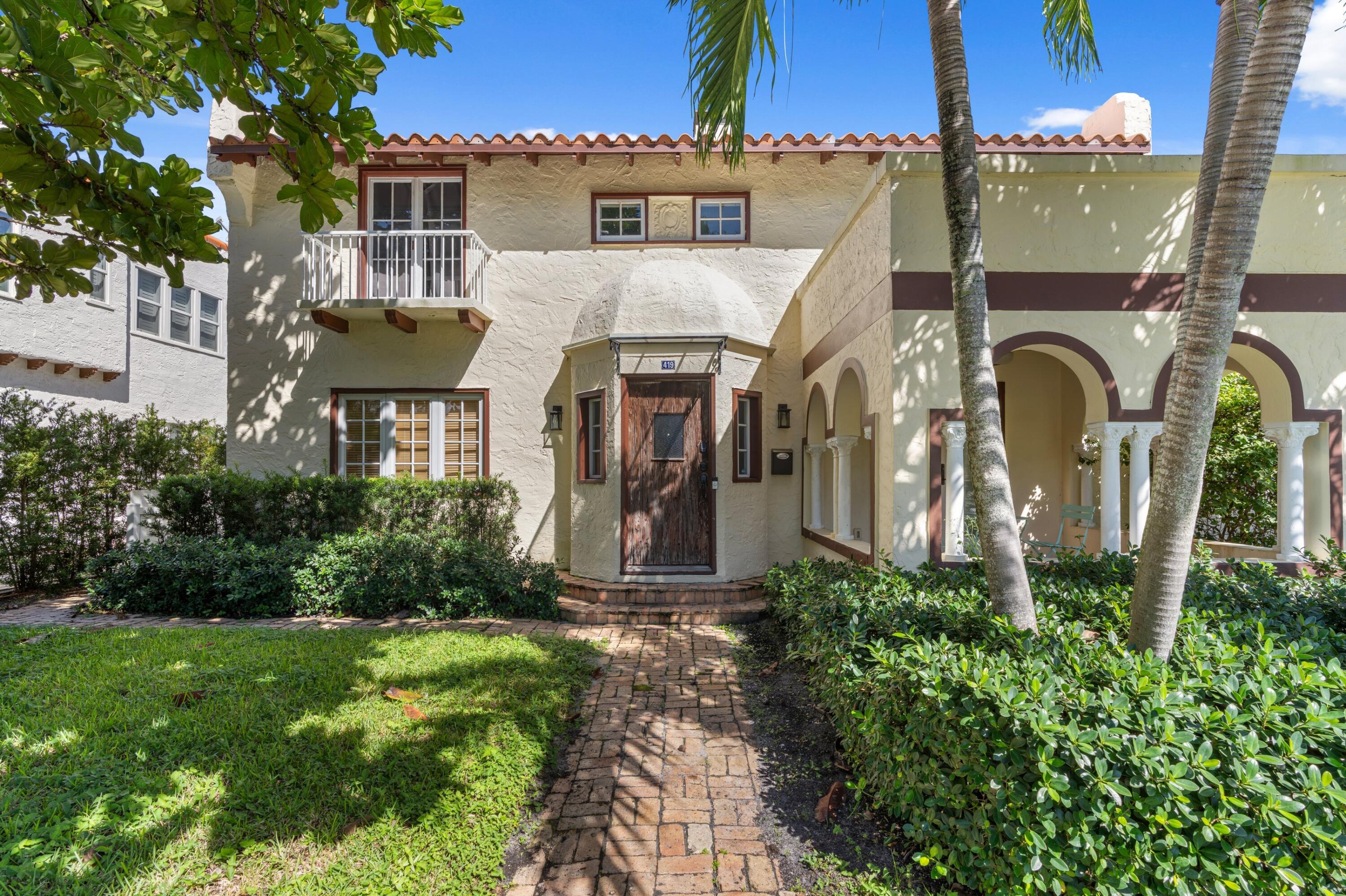 Cream stucco home with arched porch, palm trees, and a brick walkway to the entrance.
