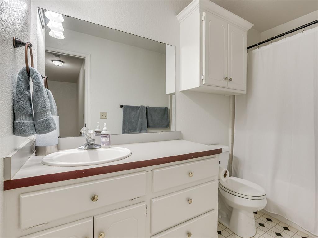 Bathroom with a white vanity and large mirror, gray towels, and black-and-white hexagonal floor tiles.