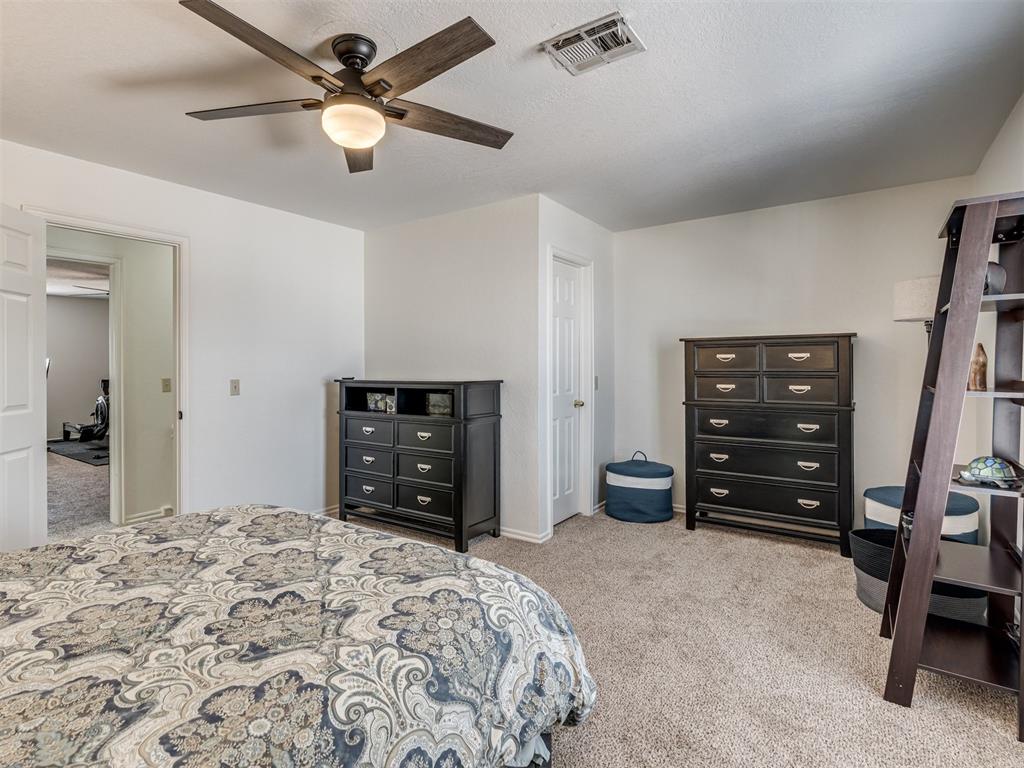 Furnished bedroom with patterned bedding, dark wood dressers, and a ceiling fan.