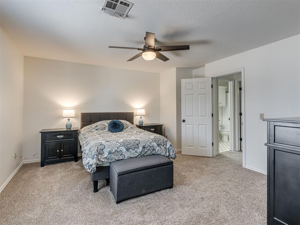 Furnished bedroom with patterned bedding, beige carpet, ceiling fan, and an open doorway to the bathroom.