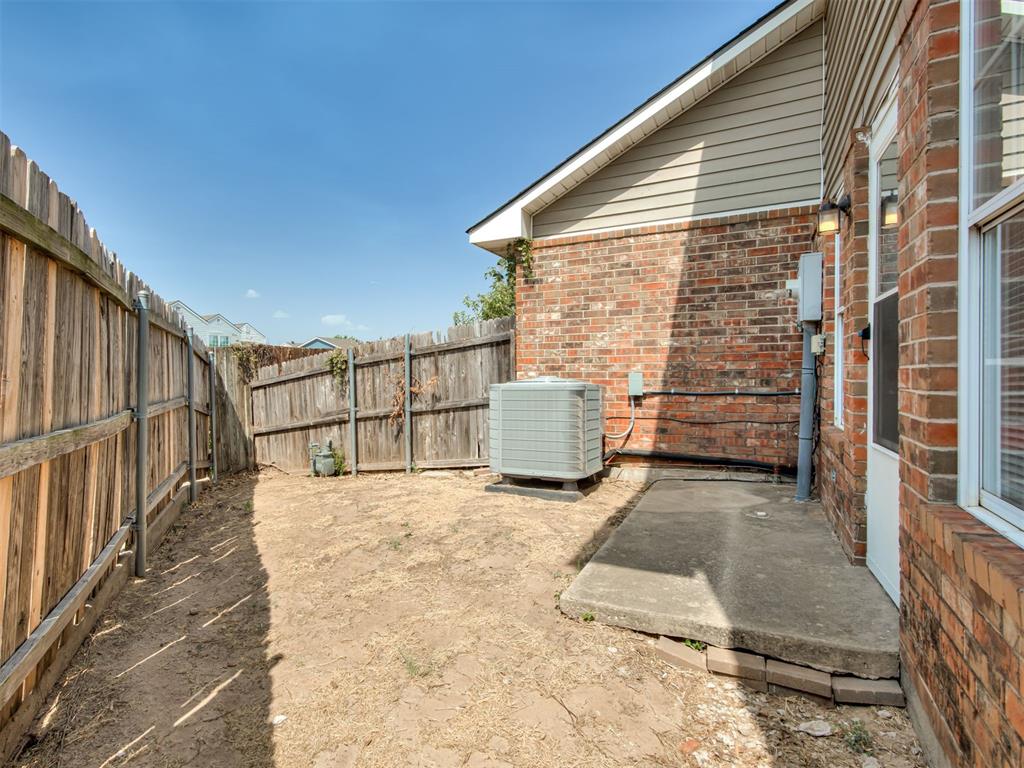 Fenced side yard beside a brick home, with a concrete patio and outdoor AC unit.