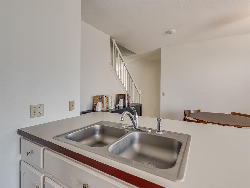 Kitchen counter with a stainless-steel double sink, overlooking a dining area and staircase.
