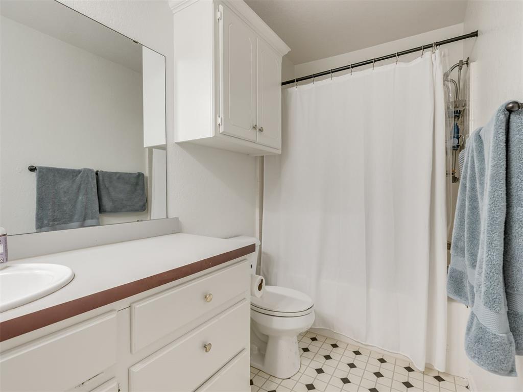 Bathroom with white vanity, mirrored cabinet, toilet, and black-and-white tiled floor.