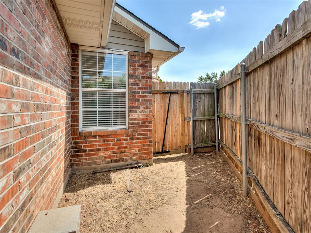 Enclosed side yard with bare ground, a brick wall, and a wooden privacy fence and gate.