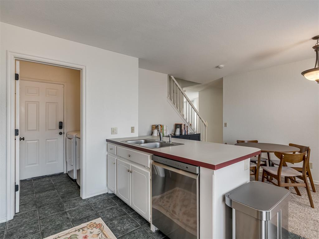 Kitchen with a white peninsula and stainless-steel dishwasher beside the dining area and staircase.